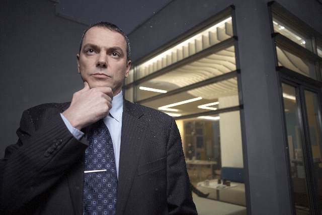 A man in a suit resting his hand on his chin in an office